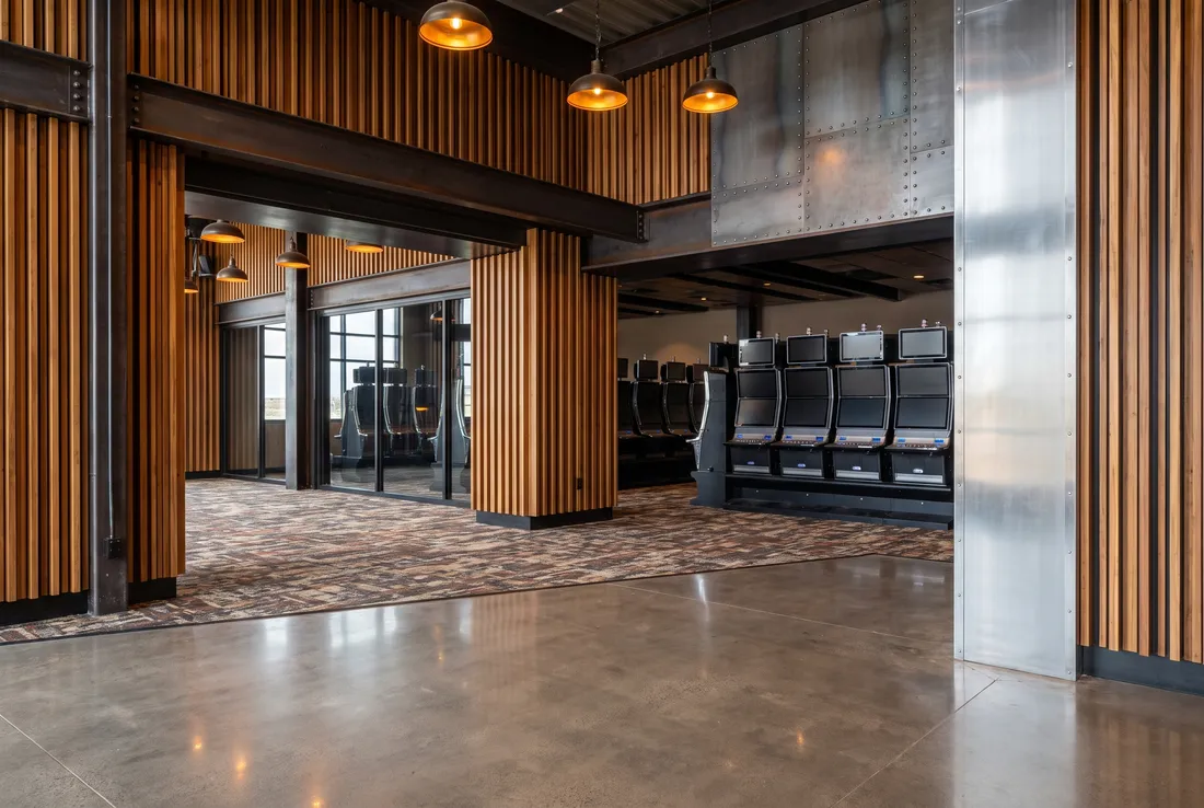 An entrance hall with vertical wood slats, dark steel beams, riveted metal panels and glass, slot machines with blank screens beyond.